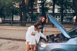 Zwei Frauen mit kaputtem Auto auf der Straße. offene Haube foto