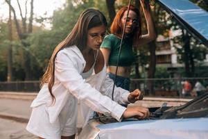 Zwei Frauen mit kaputtem Auto auf der Straße. offene Haube foto