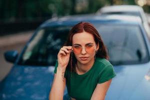 schönes Mädchen sitzt auf der Motorhaube eines blauen Autos foto