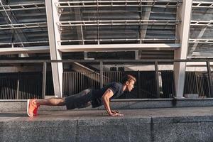 Hart Arbeiten. Junger Mann in Sportkleidung, der beim Training im Freien die Plankenposition hält foto