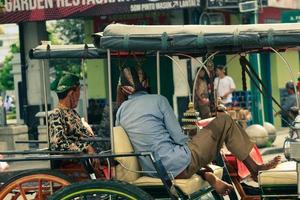 seitenansicht der zusammenwirkung des wagens oder andong fahrer auf jalan malioboro, yogyakarta. mit typisch javanesischer Batikkleidung und Blangkon-Hüten foto