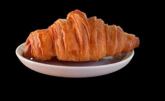 einfaches Croissant auf weißem Teller auf schwarzem Hintergrund foto