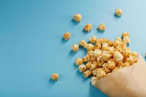 Popcorn in Karamellglasur in einem Papierumschlag auf blauem Hintergrund. foto