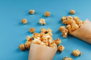 Popcorn in Karamellglasur in einem Papierumschlag auf blauem Hintergrund. foto