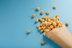 Popcorn in Karamellglasur in einem Papierumschlag auf blauem Hintergrund. foto