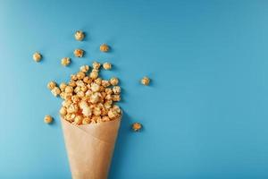 Popcorn in Karamellglasur in einem Papierumschlag auf blauem Hintergrund. foto