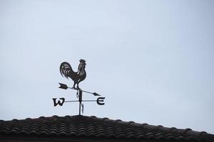 Die alte Windfahne mit einem Hahnsymbol auf dem Dach, traditionelle Technologieausrüstung zur Vorhersage und Messung des Windwetters in der Luft, Vintage-Dekoration, Windrichtungsinstrument. foto