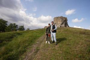 sohn mit vater trägt rucksack beim wandern in der nähe eines großen steins im hügel. pidkamin, ukraine. foto