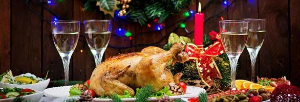 gebackener Truthahn oder Huhn. Der Weihnachtstisch wird mit einem Truthahn serviert, der mit leuchtendem Lametta und Kerzen dekoriert ist. Brathähnchen, Tisch. Weihnachtsessen. Banner foto