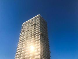 Großer hoher Stahlbeton, Paneel, monolithischer Rahmen, Rahmenblockhaus, Gebäude, Wolkenkratzer, Neubau mit Sonnenstrahlen in den Fenstern gegen den blauen Himmel foto