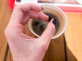 eine frau hält mit einer schönen maniküre an ihren fingern eine röhre in einer tasse schnellen schwarzen heißen starken natürlichen kaffees aus fast food in einem papierglas foto