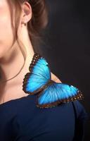 Nahaufnahme eines blauen Schmetterlings auf der Schulter eines jungen Mädchens auf dunklem Hintergrund. das konzept zerbrechlichkeit der natur foto