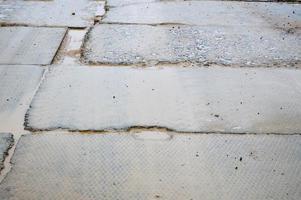 Schlechte schmutzige Betonstraße aus Blöcken und Platten mit Nähten und Rissen, die auf der Baustelle von Gebäuden und Häusern repariert werden müssen. Hintergrund zurück. Textur foto