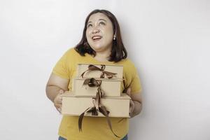 eine glückliche junge asiatische großformatige frau trägt gelbes hemd und hält geschenkbox und einkaufstasche. foto