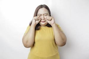 Ein Porträt einer großen asiatischen Frau, die ein gelbes T-Shirt trägt, das von weißem Hintergrund isoliert ist, sieht deprimiert aus foto