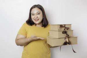 eine glückliche junge asiatische großformatige frau trägt gelbes hemd und hält geschenkbox und einkaufstasche. foto