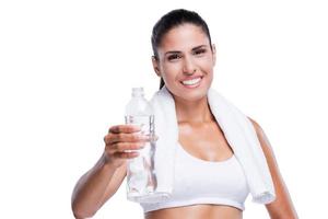 Bleiben Sie cool und hydratisiert Schöne junge Frau in weißem BH und Höschen, die eine Flasche mit Wasser hält und lächelt, während sie isoliert auf Weiß steht foto