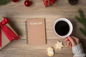 Frauenhand, die eine schwarze Kaffeetasse mit leerem Notizbuch und Weihnachtsplätzchen auf dem Tisch hält. weihnachten, frohes neues jahr, ziele, vorsatz, aufgabenliste, strategie und plankonzept foto