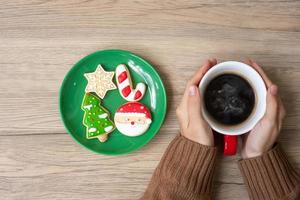 frohe weihnachten mit frauenhand, die kaffeetasse und hausgemachten keks auf dem tisch hält. weihnachtsabend, party, urlaub und frohes neues jahr-konzept foto