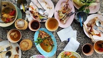 Flaches thailändisches Essen mit würzigem Papayasalat, weißen Nudeln, Knochenhuhn, Krabbensalat, Sauce und frischen Tomaten bleiben nach dem Mittagessen im Restaurant auf dem Tisch. Konzept der Lebensmittelverschwendung. foto