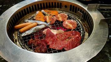 gruppe grillfleisch auf gegrilltem herd mit hotdog oder würstchen, frischer fisch, lachs, schweinefleisch, rindfleisch im koreanischen restaurant. Mittagspause und Essen foto