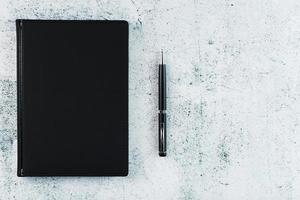 Schreibtisch mit schwarzem Notizblock und Stift auf grauem Hintergrund. foto