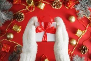 Weiße Geschenkbox mit roter Schleife in den Fäustlingen. Weihnachts- oder Neujahrsgeschenk. foto