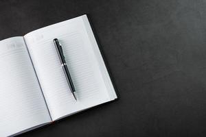 Ein offenes Notizbuch mit einem schwarzen Stift auf schwarzem Hintergrund. foto