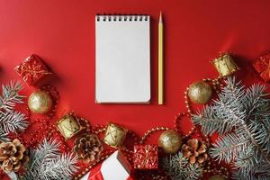 notizblock und bleistift zum schreiben von wünschen und geschenken für das neue jahr und weihnachten rund um den weihnachtsbaumschmuck auf rotem hintergrund. foto