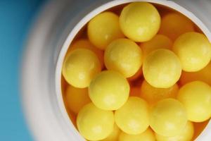 Vitamine von gelber Farbe in Form von runden Dragees in einem weißen Glas auf blauem Grund. foto