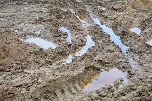 Textur einer schmutzigen, schlechten Schotterstraße Schotterstraße mit Pfützen und trocknendem Lehmschlamm mit Rissen und Furchen. Offroad. der Hintergrund foto