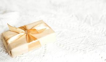 Schachtel mit Weihnachtsgeschenk in hellem Papier ist mit einem goldenen Band auf weißem gestricktem Hintergrund mit Dekor gebunden. goldene Girlande aus Sternen. Neujahr. Glückwunsch, Überraschung. Platz für Text foto