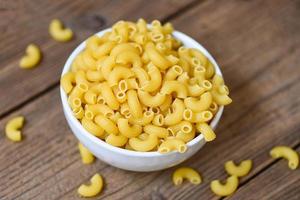 rohe makkaroni ungekochte köstliche pasta oder penne-nudeln - makkaroni auf schüssel und hölzernem hintergrund, draufsicht foto
