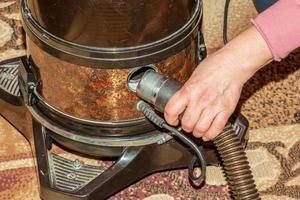 das Reinigen des Teppichs mit einem Staubsauger mit Wasserfilter. Die Hand einer Frau führt einen Staubsaugerschlauch in den Luftauslass ein foto