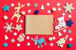 draufsicht auf notizbuch, weihnachtsspielzeug und dekorationen auf rotem weihnachtshintergrund. neujahrszeitkonzept foto