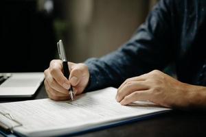 geschäftsmann unterzeichnet dokumente mit einem stift, der den unterzeichnungsvertrag und die partnerschaft auf dem schreibtisch erstellt. foto