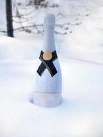 eine weiße flasche champagner, die im weißen frostigen schnee vergraben ist, bereit für partyfeiern, die grüße der jahreszeit, frohe feiertage, weihnachten, neujahr foto