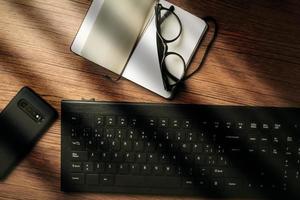 Blick von oben auf den hölzernen Vintage-Schreibtisch mit Schwerpunkt auf Laptop mit Notizblock, Smartphone und Brille. Arbeitsplatz. Von zuhause aus arbeiten. Schreibtisch. foto