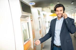 der kaukasische mann benutzt eine transportkarte am fahrkartenautomaten für die reise mit dem sky train in der hauptverkehrszeit, während er das smartphone zum sprechen mit seinem freund verwendet. foto