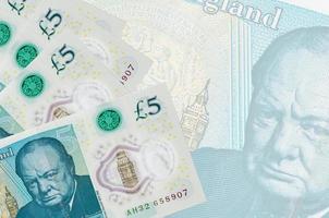 5 britische Pfund-Scheine liegen im Stapel auf dem Hintergrund einer großen halbtransparenten Banknote. abstrakter betriebswirtschaftlicher hintergrund foto