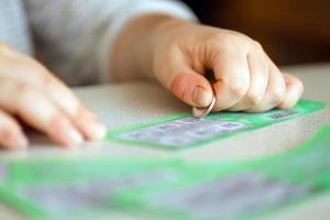 Nahaufnahme der Silbermünze in der Hand des Spielers, der eine gefälschte Lotteriekarte kratzt. lotteriespielkonzept, kratzkartenlotterie foto