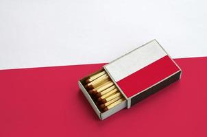 Die polnische Flagge wird in einer offenen Streichholzschachtel gezeigt, die mit Streichhölzern gefüllt ist und auf einer großen Fahne liegt foto