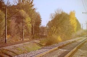 herbstliche Industrielandschaft. Eisenbahn, die sich zwischen grünen und gelben Herbstbäumen in die Ferne zurückzieht foto