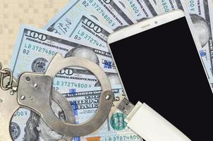 100 US-Dollar-Scheine und Smartphone mit Polizeihandschellen. Konzept von Hacker-Phishing-Angriffen, illegalem Betrug oder weicher Verteilung von Malware foto