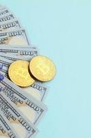 goldene bitcoins und hundertdollarscheine liegen auf hellblauem hintergrund foto