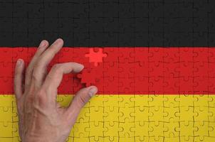 die deutschlandflagge ist auf einem puzzle abgebildet, das die hand des mannes zum falten vervollständigt foto