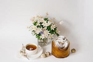 Osterkarte. ein Kuchen, eine Tasse Tee, Primeln in einer Vase und Wachteleier auf hellem Hintergrund foto