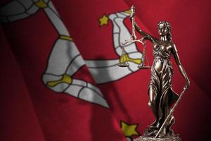 isle of man-flagge mit statue der dame justiz und gerichtswaage im dunklen raum. Konzept von Urteil und Bestrafung foto