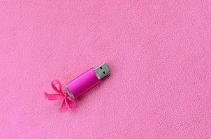 Eine leuchtend rosa USB-Flash-Speicherkarte mit einer rosa Schleife liegt auf einer Decke aus weichem und pelzigem hellrosa Fleece-Stoff. klassisches weibliches Geschenkdesign für eine Speicherkarte foto