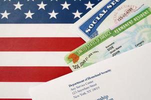 United States Permanent Resident Green Card von DV-Lotterie mit Sozialversicherungsnummer liegt mit Uscis-Umschlag auf US-Flagge foto